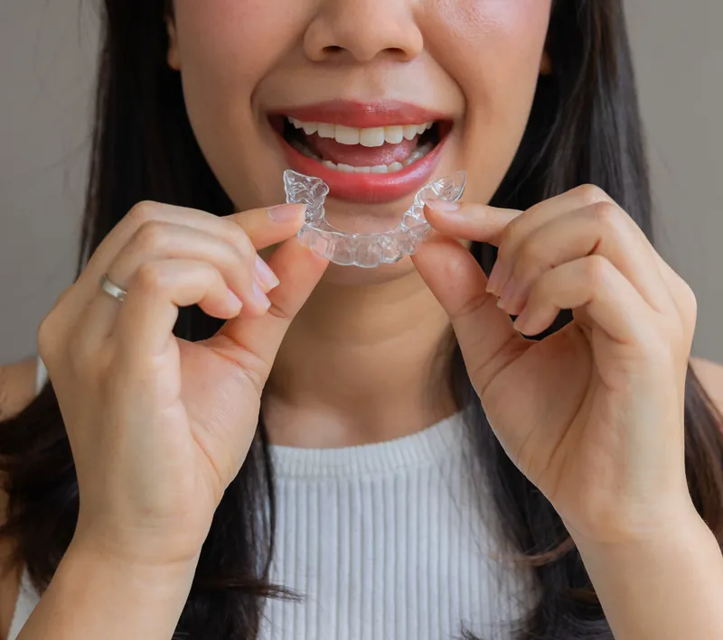 Femme qui tient un aligneur transparent devant son sourire